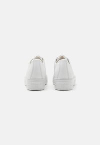 Baskets blanches avec un dessus en cuir lisse, semelle plate et un branding subtil au niveau du talon. Design minimaliste avec une forme épurée et fluide.