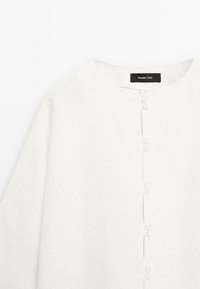 Chemise en lin blanc avec un col rond, fermeture à boutons sur le devant et tissu légèrement texturé. Étiquette de la marque : Massimo Dutti.