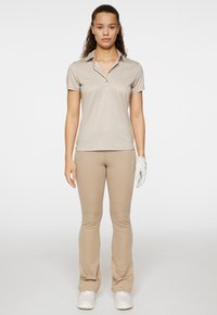 Polo beige con un motivo sottile, maniche corte e colletto, abbinato a pantaloni beige aderenti e guanto da golf bianco.