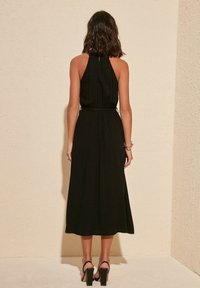 Zwarte halterjurk met een aangesloten lijfje en een vloeiende midi-rok, voorzien van een keyhole rug, gedragen met zwarte block-heeled sandalen.