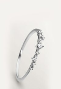 Anillo delgado de plata con una fila de pequeños diamantes brillantes engastados en la mitad superior de la banda sobre un fondo neutro.