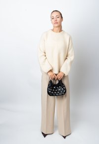 Kremasti, pahuljasti džemper s spuštenim ramenima, upareni s bež širokim hlačama. Crna satenska torba s metalnim zakovicama u ruci.