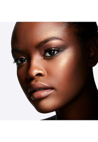 Close-up of a face featuring smooth dark skin, defined cheekbones, natural makeup with shimmering highlights, and full, neutral-toned lips.