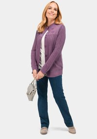 Paarse gebreide cardigan met een structuurpatroon, met knopen aan de voorkant. Draagt over een witte top, gecombineerd met blauwe jeans en een grijze handtas.