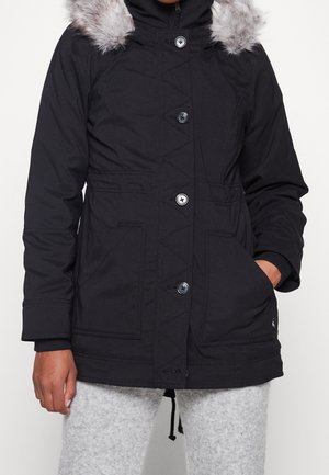 Zwarte parka jas met een nepbont capuchon, voorzien van een knoopsluiting, twee voorzakken en diagonale stikdetails op het lichaam.