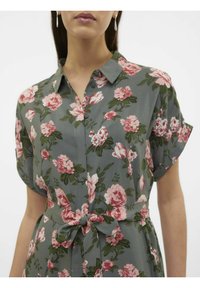 Vestito floreale in tessuto verde con fiori rosa, maniche corte e dettaglio in vita legato. Presenta una patta con bottoni e una consistenza morbida.
