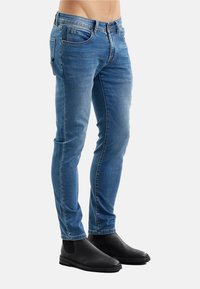 Jeans di denim blu con vestibilità slim, dotati di cinque tasche, finitura sbiadita e dettagli di cuciture. Abbinati a stivaletti in pelle nera.