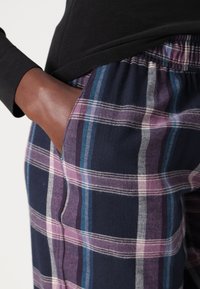 Pantalons en coton à carreaux avec un fond bleu marine et des rayures violettes, bleues et blanches, taille élastique et détail de poches latérales.