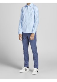 Světle modrá košile s dlouhým rukávem a knoflíkovým zapínáním, spárovaná s modrými kalhotami a bílými teniskami s vícebarevnými akcenty.