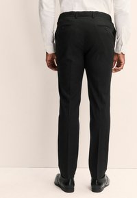Pantalones negros ajustados de corte recto, con bolsillos traseros abotonados y tejido suave. Combinados con zapatos de vestir negros.