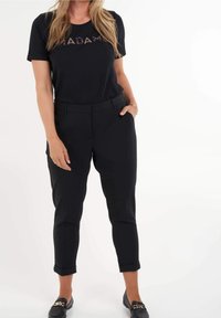 Camiseta negra con la palabra "MADAME" en una impresión metálica en contraste, combinada con pantalones negros de cintura alta y mocasines negros. Tejido suave, diseño ajustado.