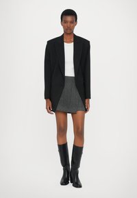 Svart oversized blazer over en hvit topp, kombinert med et grått tweedskjørt og høye, svarte skinnstøvler. Klar, minimalistisk design.