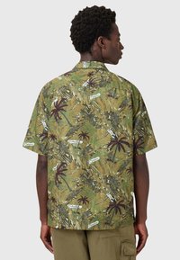 Κοντομάνικο πουκάμισο με πράσινο, μοτίβο που περιλαμβάνει φοίνικες και κείμενα. Χαλαρή εφαρμογή με γιακά και κουμπί.