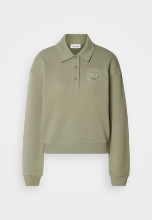 Sweatshirt polo verde-azeitona cortado com mangas longas, dois botões e um logo bordado redondo no peito. Tecido com textura macia.