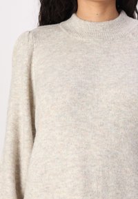 Pull en maille gris clair avec un col montant et un tissu texturé. Doté de manches longues et d'une subtile variation de couleur sur toute la surface.