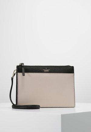 Rechthoekige polstasje met een beige onderste paneel, zwart bovenste paneel, gouden ritssluiting en afneembare zwarte band op een wit platform.