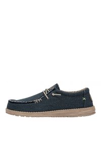 Chaussures slip-on en toile bleue texturée avec une semelle en caoutchouc beige, des coutures contrastantes et un petit logo vert sur le côté.