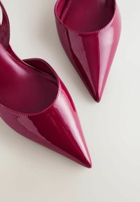 Escarpins slingbacks en cuir verni rouge avec bouts pointus et découpes courbes, dotés d'une finition brillante et de détails cousus le long des bords.
