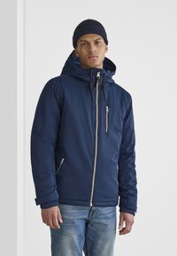 Navy blue zip-up jacket with a hood, featuring elastic cuffs, side pockets, and decorative drawstrings. Pair with blue jeans.