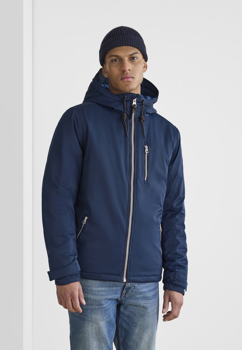 Navy blue zip-up jacket with a hood, featuring elastic cuffs, side pockets, and decorative drawstrings. Pair with blue jeans.