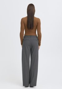 Hnedý top s dlhým rukávom kombinovaný s vysokými šedými nohavicami so širokými nohavicami, ktoré majú textúrovanú tkaninu a decentné detaily zadného vrecka.