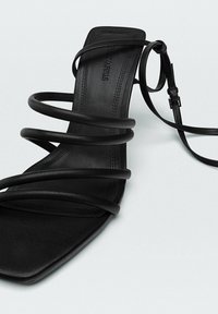 Zwarte hak sandaal met vijf dunne banden, een vierkante neusdesign, een gladde lederen textuur en een enkelbandje met een gesp voor aanpassing.