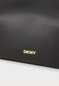Svart teksturert lærveske med et gullfarget metall "DKNY"-logo. Designet er stilrent uten synlige mønstre eller tilleggselementer.