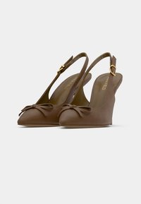 Καφέ γόβες slingback με μυτερή μύτη και μικρές φιόγκους μπροστά, με χρυσές πόρπες, τοποθετημένες σε λευκό φόντο.