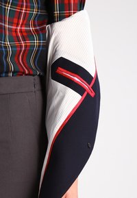 Chemise sur mesure avec un motif à carreaux multicolores, présentant une manche rayée blanche avec des accents contrastants en bleu marine et rouge.