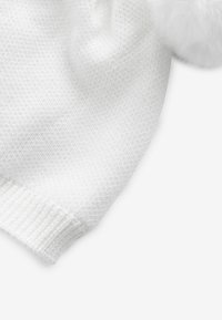 Bonnet en tricot blanc avec un motif texturé et un pompon blanc duveteux sur le dessus ; il présente un revers côtelé pour plus de détail.