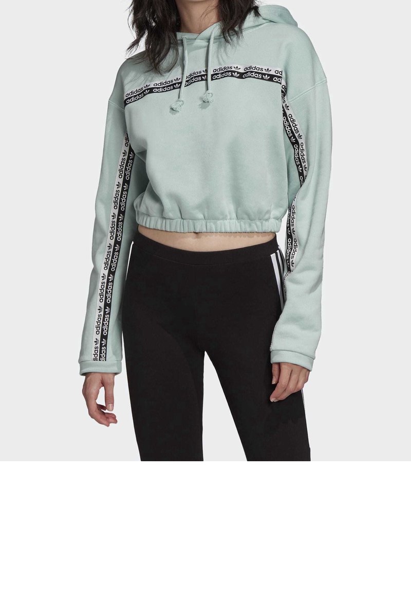 Croppad mintgrön hoodie med dragsko. Har svart märkestape längs ärmarna och ett horisontellt mönster på bröstet. Mjuk, fleeceaktig textur.