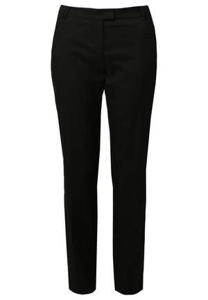 Kobieta ubrana w biały top z czarną lamówką, czarne spodnie i czarne botki, trzymająca czarną i srebrną kopertówkę.