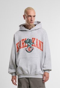 Gray sweatshirt with a large red "KARL KANI" logo, an eagle graphic, and drawstring hood. Features ribbed cuffs and a front pocket.