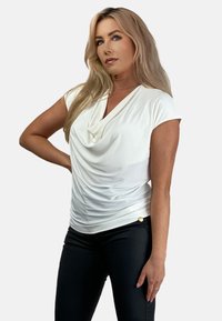 Biała bluzka z drapowaniem, z krótkimi rękawami, dekoltem w kształcie czołgu i marszczonym materiałem w talii. Połączona z czarnymi dopasowanymi spodniami i złotymi akcentami.