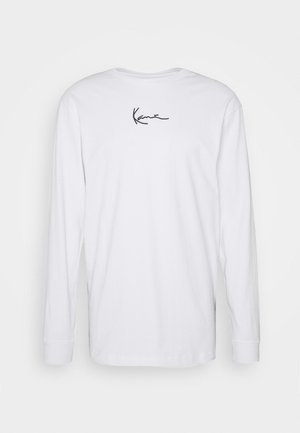 Camiseta blanca de manga larga con un pequeño logo en cursiva negra centrado cerca de la parte superior de la espalda, mostrada sobre un fondo liso.