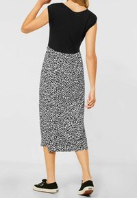 Musta toppi lyhyillä hihoilla ja pyöreällä kaula-aukolla, yhdistettynä polvipituiseen musta-valkoiseen lehtikuvioiseen hameeseen. Mustat lenkkarit.