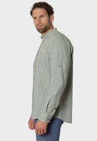 Camisa verde claro de botones, hecha de tela texturizada, con cuello, mangas largas y puños abotonados.