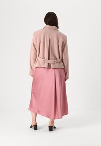 Roosa tekstuuriga jakkerihmaga. Ühendatud siledast kangast roosa põlvepikkuse seeliku ja mustade kontsaga sandaalidega. Seljaview.