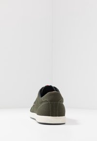 Gröna kanvassneakers med en texturerad yta, vit gummisula och marinblå foder. Har röda och vita logofraktioner på sidan.