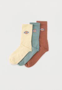 Τρία διπλωμένα πλήρως καλτσάκια Dickies σε μπεζ, πράσινο-μπλε και σκουριασμένο χρώμα, καθένα με κυκλικό λογότυπο της μάρκας στην μανσέτα.