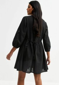 Zwarte linnen jurk met driekwart mouwen, bloemenborduursel op de mouwen, een getailleerde taille met een strik, en een uitlopende rok.