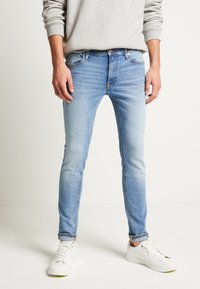 Calças skinny de denim em azul claro, apresentando um efeito desbotado, design de cinco bolsos e um leve efeito de desgaste nas coxas.