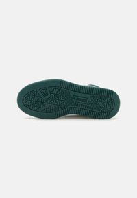 Semelle de chaussure vert foncé avec des rainures à motifs et le logo "PUMA" embossé au centre sur un fond clair uni.