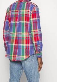 Camicia a quadri multicolore con motivi verdi, blu, rossi e gialli; maniche lunghe e orlo curvo; in cotone.