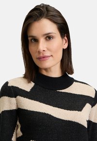 Black and beige knit sweater with a patterned design; features a high, ribbed neckline and textured fabric.