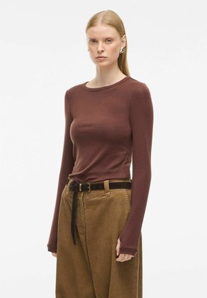 Bruine lange mouwen top met een aansluitend ontwerp, gecombineerd met ruime beige corduroy broek en een zwarte riem. Soepele textuur en ronde halslijn.