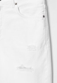 Jeans de denim blanco con un diseño desgastado y desgarrones deshilachados en la parte delantera. Incluye bolsillos estándar y herrajes metálicos.