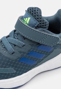 Blauwe sportieve schoen met een bovenwerk van mesh, klittenbandsluiting en veters. Beschikt over een textuurstof en drie blauwe strepen aan de zijkant. Witte zool.