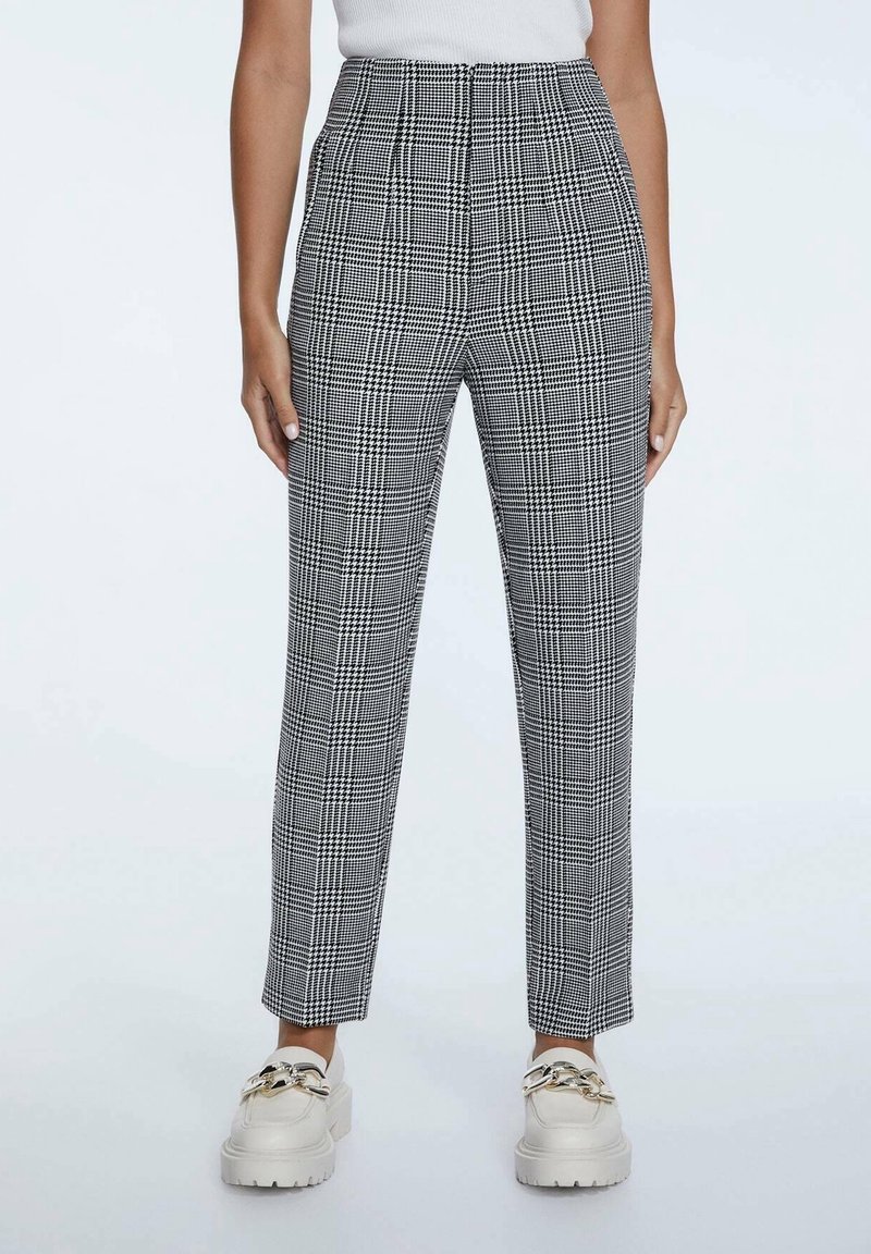 Hoge taille geplooide broek met een zwart-wit geruite print, getailleerde pasvorm en een soepele stoftextuur. Gecombineerd met chunky witte loafers.