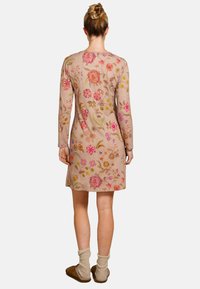 Langarm bloemenjurk in beige met multicolore borduursels. Heeft een ronde halslijn en een relaxte pasvorm, gecombineerd met comfortabele sokken en slippers.